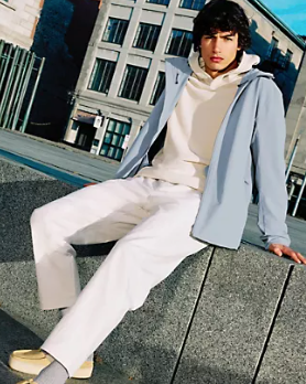 A man sitting wearing a Lululemon outfit feating a light blue jacket, cream hoodie and white pants