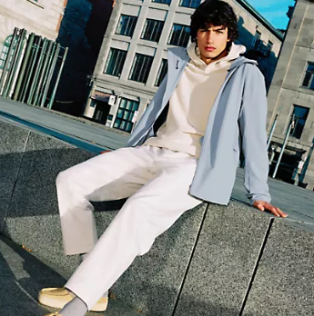 A man sitting wearing a Lululemon outfit feating a light blue jacket, cream hoodie and white pants