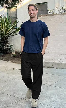 A man walking while wearing Outdoor Voices navy blue shirt and black pants