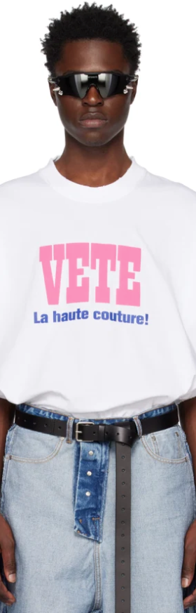 A man wearing a Vetements outfit featuring a white VETE t-shirt and blue jeans