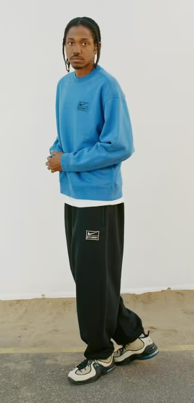 A man walking and wearing a blue Nike sweatshirt and black sweatpants