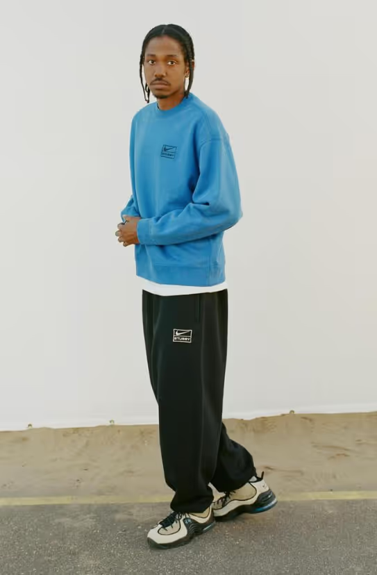 A man walking and wearing a blue Nike sweatshirt and black sweatpants