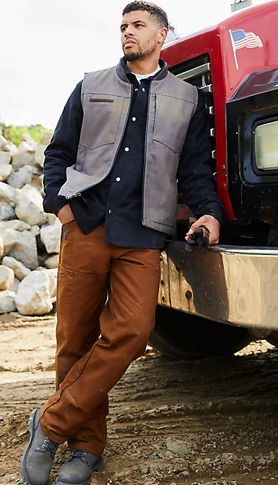 A man wearing a wrangler vest, button up and brown pants