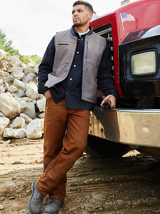 A man wearing a wrangler vest, button up and brown pants