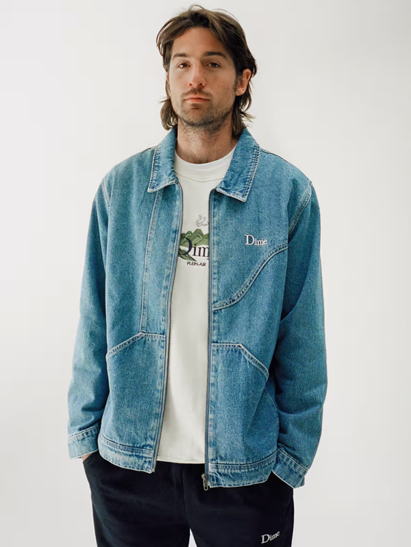 A man wearing a Dime denim jacket and a white t-shirt and navy blue pants