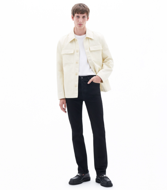 A man wearing a cream Filippa K overshirt, a white t-shirt and black slacks