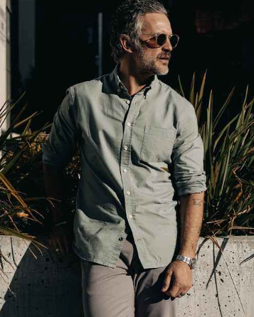 A man wearing a Taylor Stitch olive long-sleeve button up, grey pants and sunglasses