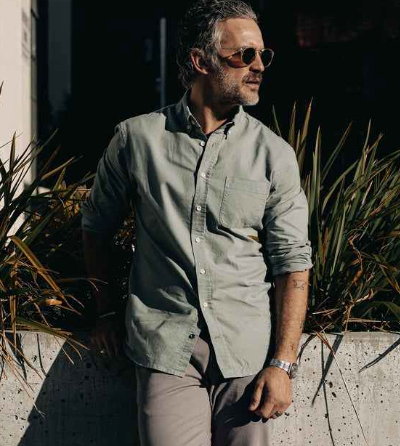 A man wearing a Taylor Stitch olive long-sleeve button up, grey pants and sunglasses