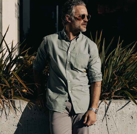 A man wearing a Taylor Stitch olive long-sleeve button up, grey pants and sunglasses