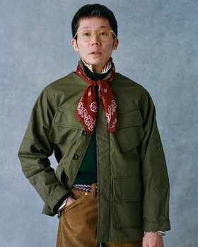 A man wearing a Drake's green coat, red bandana and brown pants