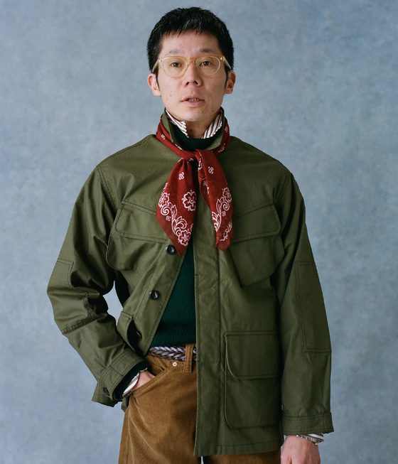 A man wearing a Drake's green coat, red bandana and brown pants