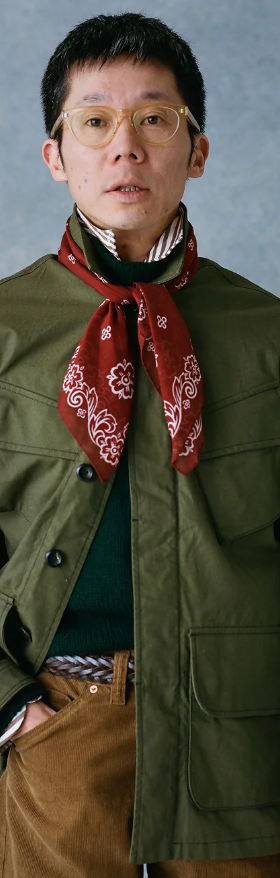 A man wearing a Drake's green coat, red bandana and brown pants