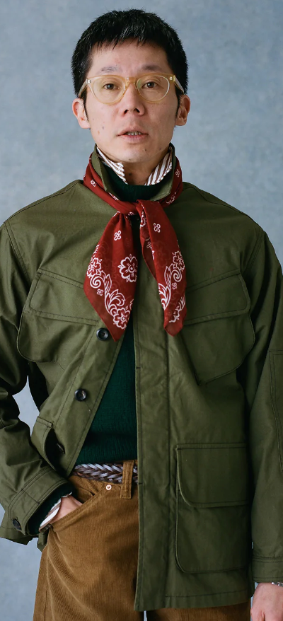 A man wearing a Drake's green coat, red bandana and brown pants