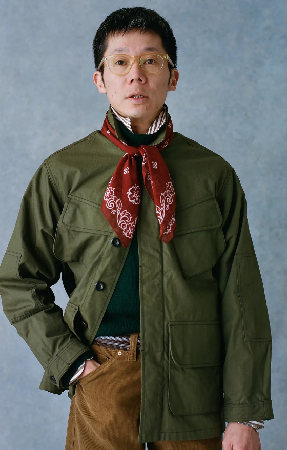 A man wearing a Drake's green coat, red bandana and brown pants