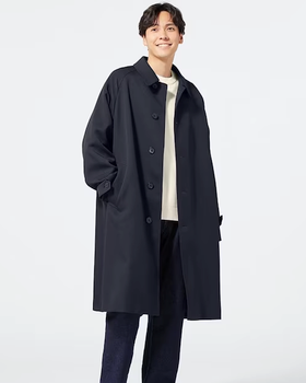 A man wearing a minamilist Gu navy blue overcoat, with a white shirt and navy blue pants