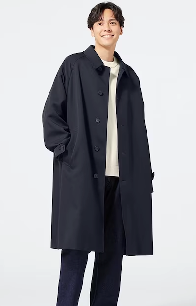 A man wearing a minamilist Gu navy blue overcoat, with a white shirt and navy blue pants