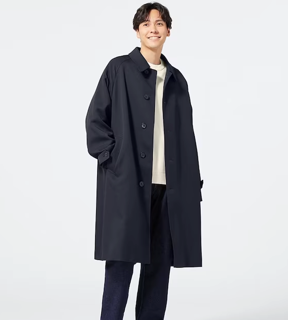 A man wearing a minamilist Gu navy blue overcoat, with a white shirt and navy blue pants