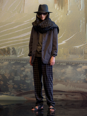 A man wearing a full Undercover outfit with a black jacket and black plaid pants with a matching scarf