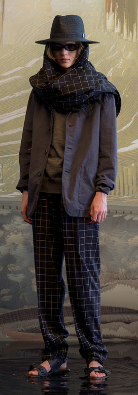 A man wearing a full Undercover outfit with a black jacket and black plaid pants with a matching scarf