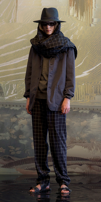 A man wearing a full Undercover outfit with a black jacket and black plaid pants with a matching scarf