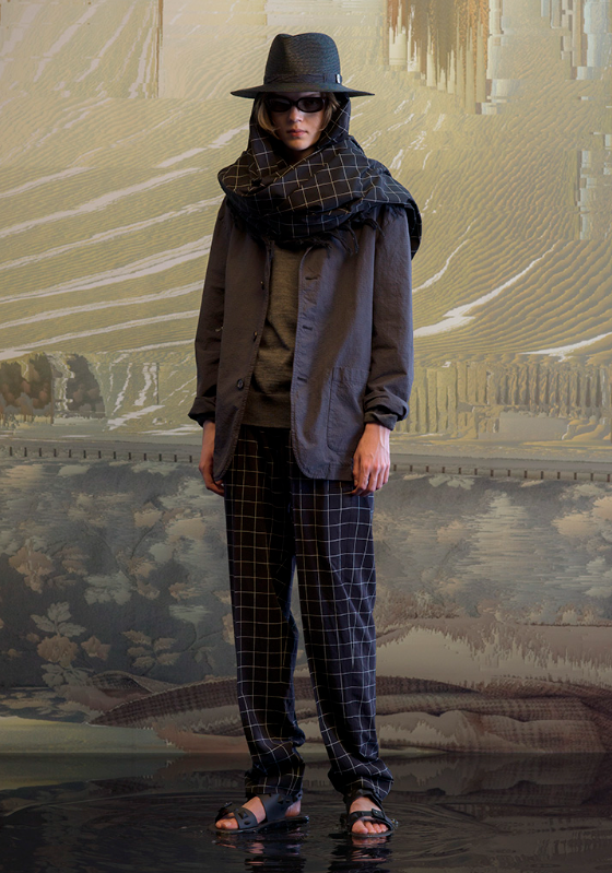 A man wearing a full Undercover outfit with a black jacket and black plaid pants with a matching scarf