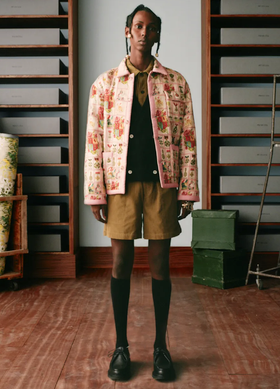 A man wearing a pink floral print Bode jacket, brown shorts and high black socks