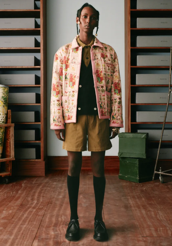 A man wearing a pink floral print Bode jacket, brown shorts and high black socks