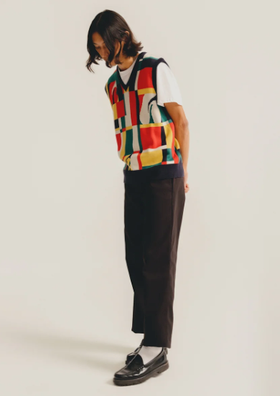 A man wearing a HUF vest in the style of Ferris Bueller with black slacks and black loafers