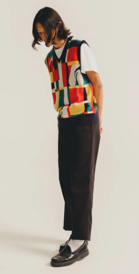 A man wearing a HUF vest in the style of Ferris Bueller with black slacks and black loafers