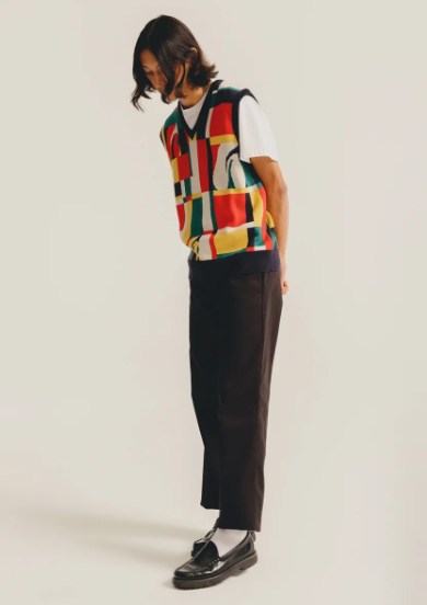 A man wearing a HUF vest in the style of Ferris Bueller with black slacks and black loafers