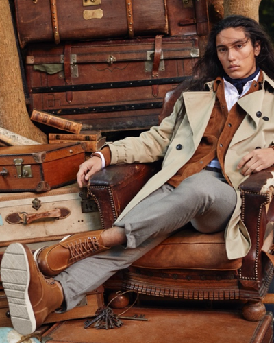 A man sitting in a chair wearing a Banana Republic trench coat, a brown jacket underneath and brown shoes