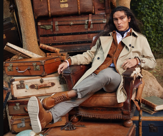 A man sitting in a chair wearing a Banana Republic trench coat, a brown jacket underneath and brown shoes