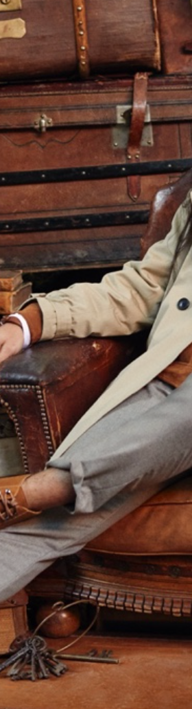 A man sitting in a chair wearing a Banana Republic trench coat, a brown jacket underneath and brown shoes