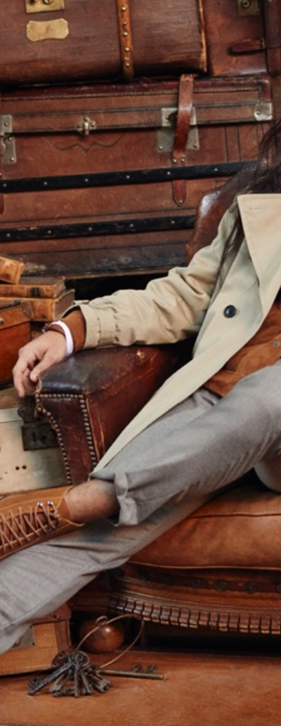 A man sitting in a chair wearing a Banana Republic trench coat, a brown jacket underneath and brown shoes