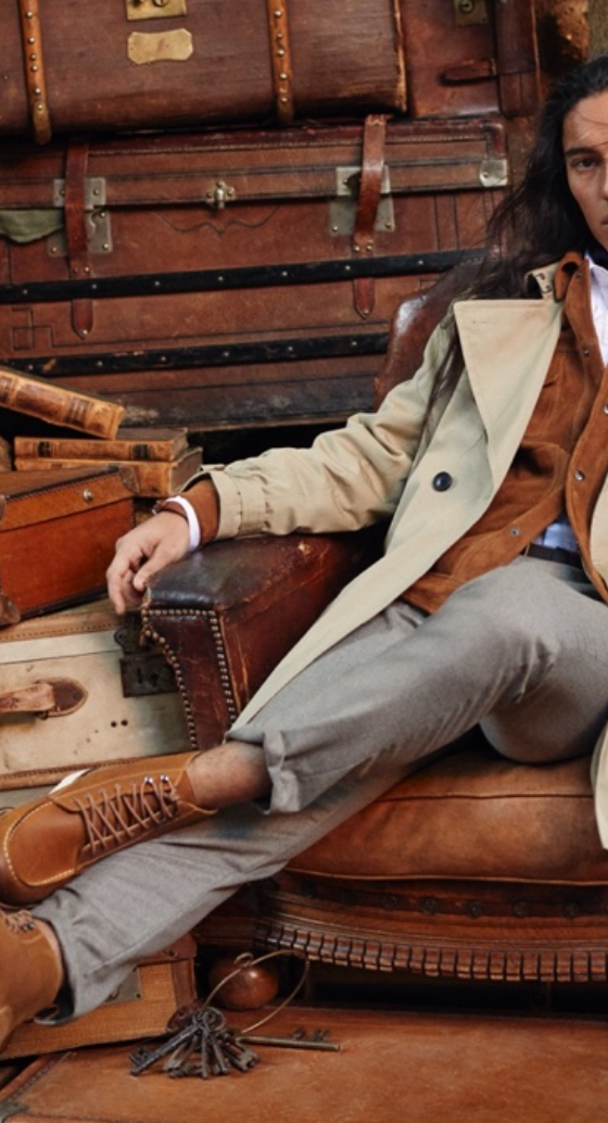 A man sitting in a chair wearing a Banana Republic trench coat, a brown jacket underneath and brown shoes