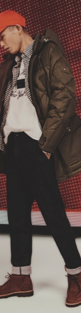 A man wearing a red Tommy Hilfiger hat, brown winter coat and jeans