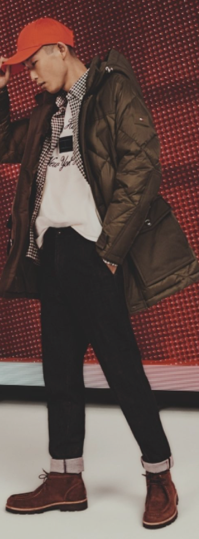 A man wearing a red Tommy Hilfiger hat, brown winter coat and jeans