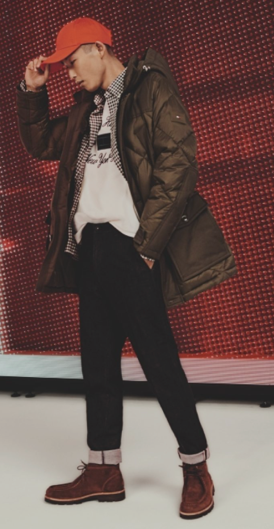 A man wearing a red Tommy Hilfiger hat, brown winter coat and jeans