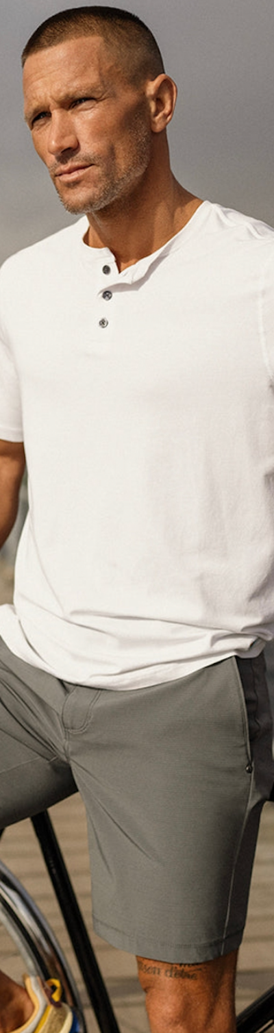 A man wearing a Vuori outfit sitting on a bridge with a white shirt and dark grey shorts
