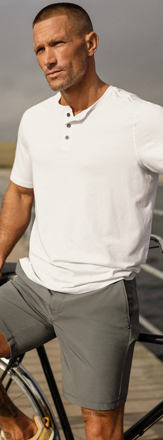 A man wearing a Vuori outfit sitting on a bridge with a white shirt and dark grey shorts