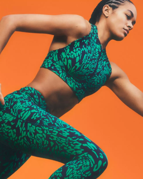 A woman mid-sprint wearing a colorful green Sweaty Betty athletic spandex