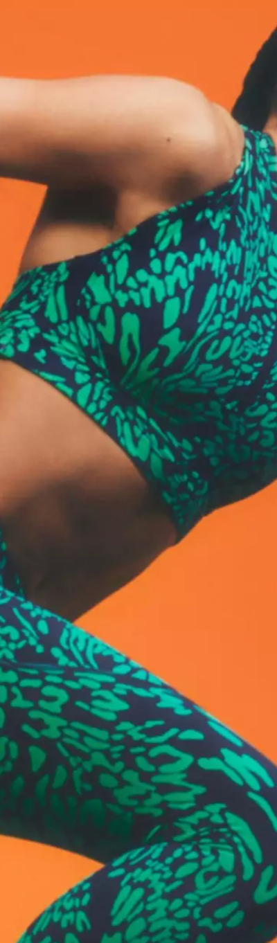 A woman mid-sprint wearing a colorful green Sweaty Betty athletic spandex
