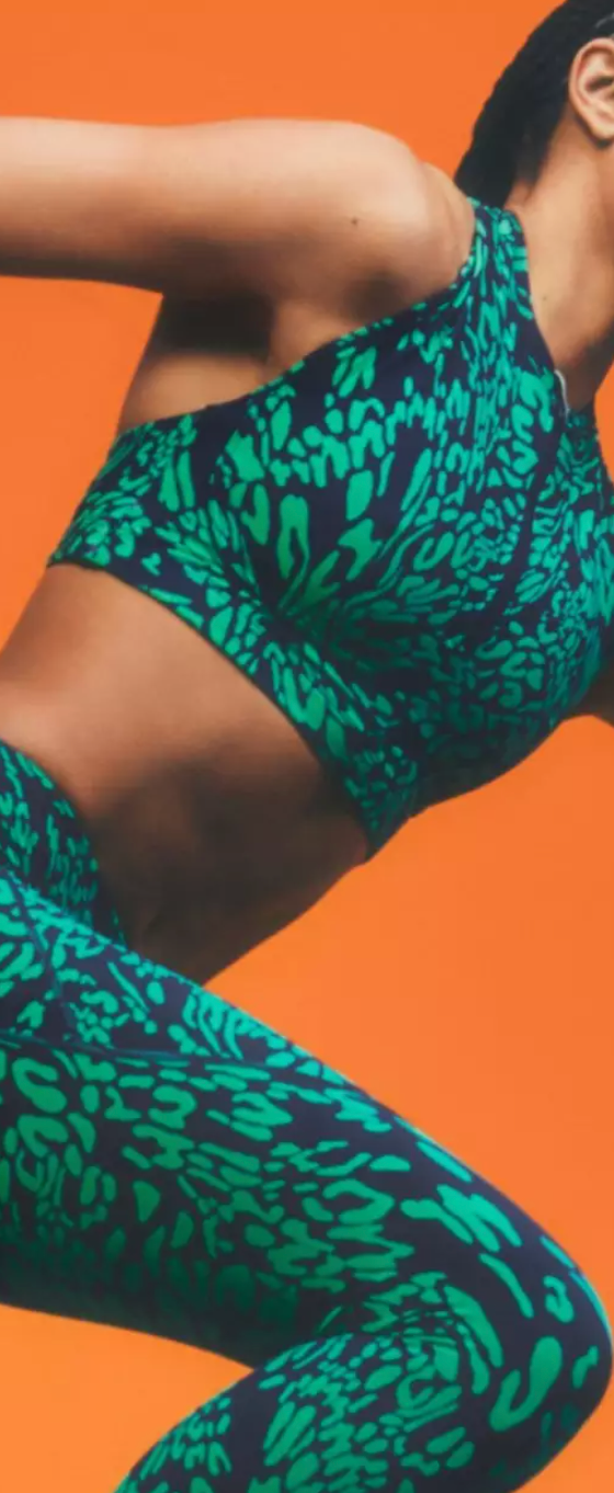 A woman mid-sprint wearing a colorful green Sweaty Betty athletic spandex