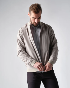 A man zipping up his Rhone coat overtop a grey button up