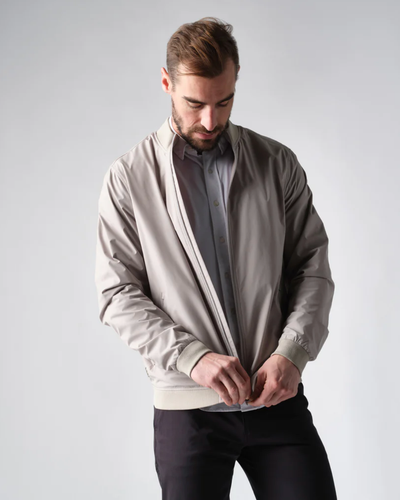 A man zipping up his Rhone coat overtop a grey button up