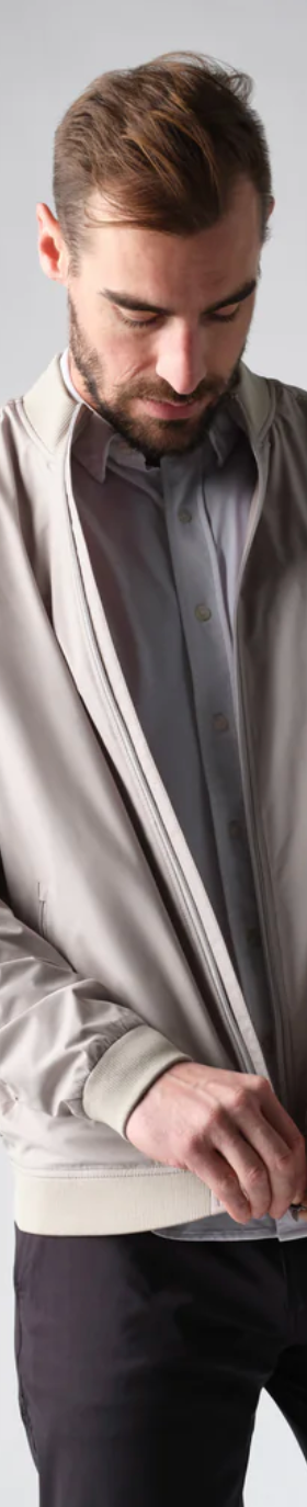A man zipping up his Rhone coat overtop a grey button up