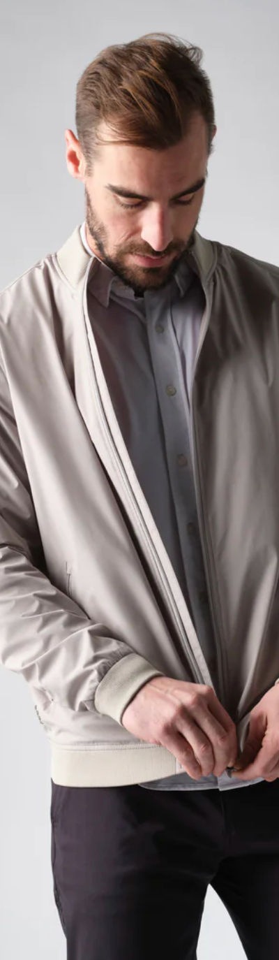 A man zipping up his Rhone coat overtop a grey button up