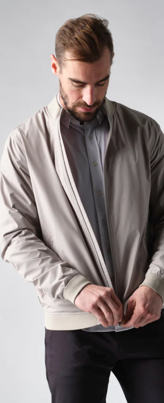 A man zipping up his Rhone coat overtop a grey button up