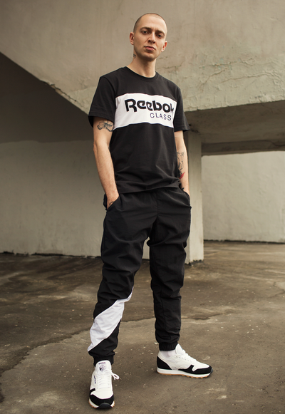 A man standing wearing a black and white Reebok Classics outfit with matching sneakers