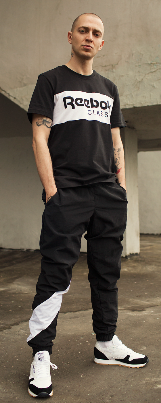 A man standing wearing a black and white Reebok Classics outfit with matching sneakers